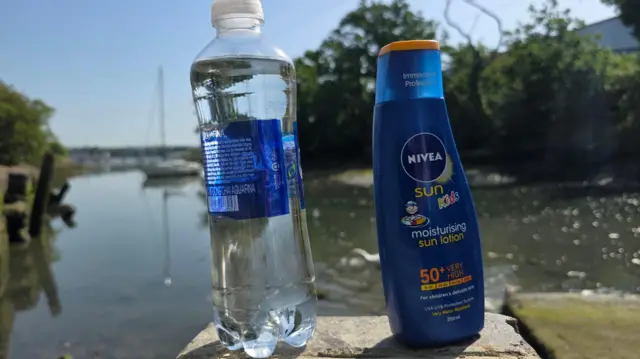 A bottle of water and a bottle of Nivea sunscreen standing side by side with a body of water in the background.