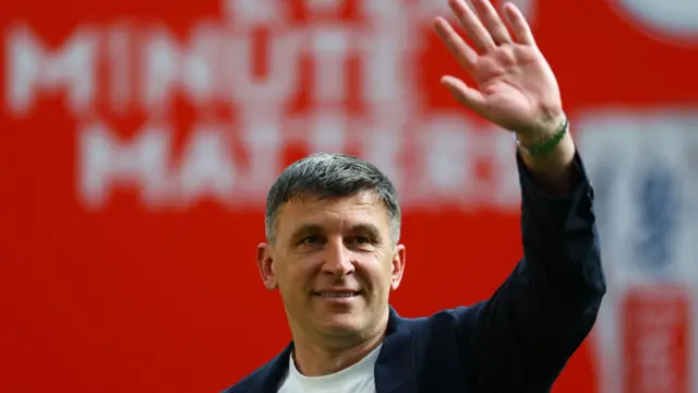 Sergej Jakirovic, a man with short cropped greying dark hair, wears a white t-shirt and blue jacket as he waves to fans at Wembley.