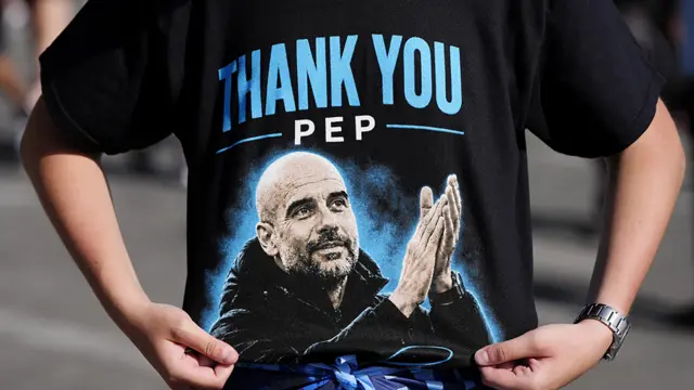 A Manchester City fan wears a black t-shirt which says 'Thank you Pep' with an image of the manager Pep Guardiola clapping