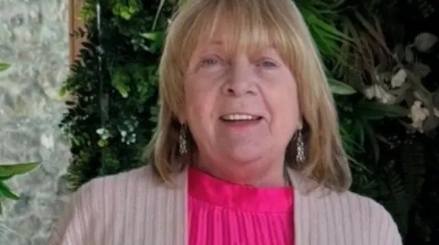 Hazel looking into the camera lesnse, she has shoulder length blonde hair and is wearing a pink swetare