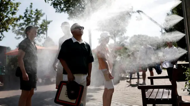 People stand under outdoor mist spray to cool off on sunny day.