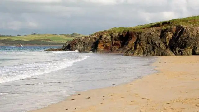 Part of Tregirls Beach near Padstow in Cornwall. The waves are crashing into the sand. A craggy area of the coast is in the background.