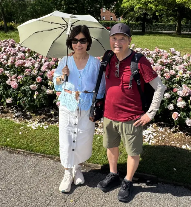 An older man and woman, holding an umbrella, in a park.