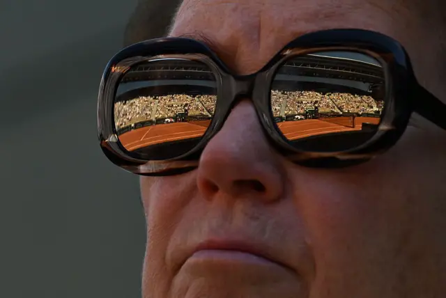 A man's sunglasses reflect the clay court