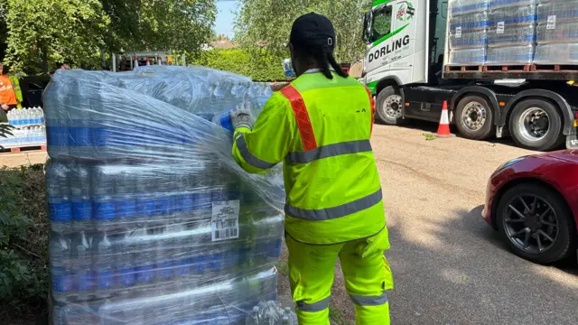 A man in a high-vis yellow jacket unloads bottled water on a crate