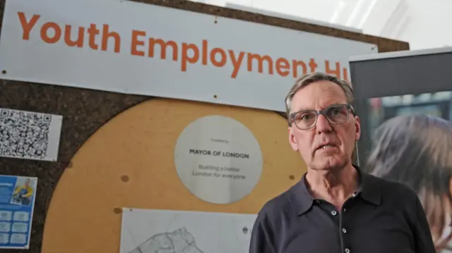 Alan Milburn stands in front of a yellow sign at a press conference about the report.
