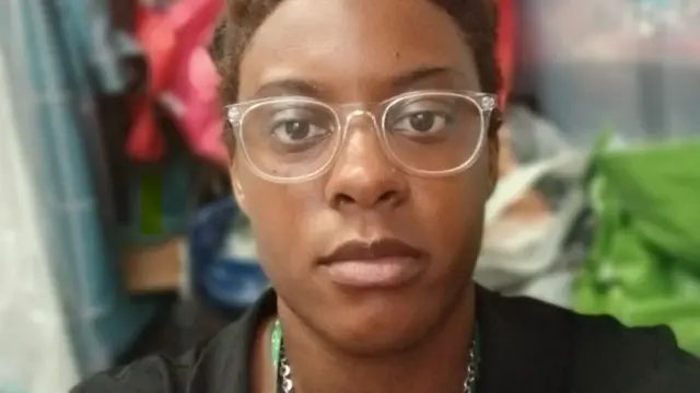 Savanna takes a selfie. She is wearing white framed glasses and a black top as well as a silver necklace