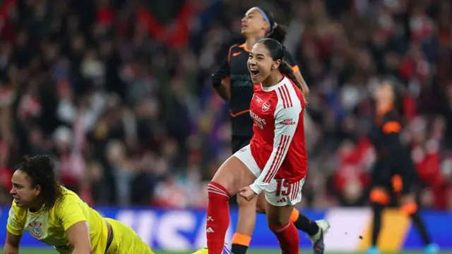 Olivia Smith celebrates and runs on the pitch next to a goalie who is laying on the floor resting up on their hands and a player of the opposition stands behind looking frustrated
