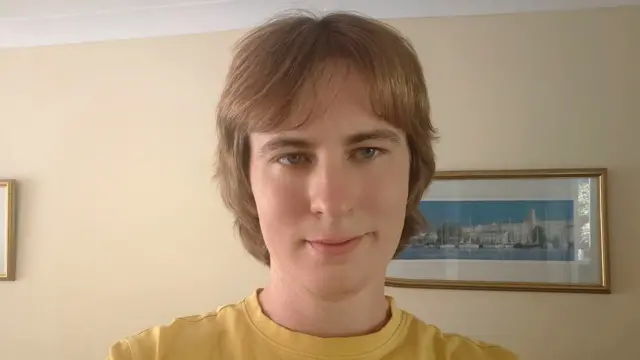 Man wearing a yellow t-shirt smiles as he looks towards the camera