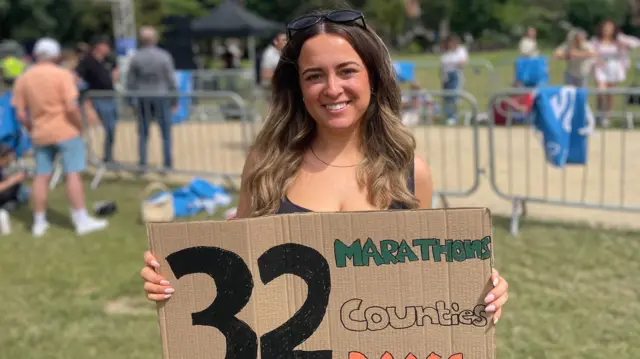 A woman holding a cardboard sign saying 32 marathons, countries, days.