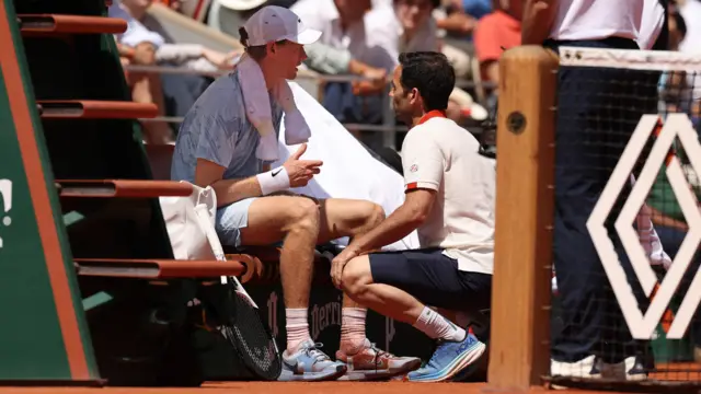 Jannik Sinner speaks to the trainer while sitting in his chair