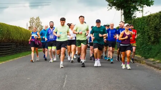 A group of runners wearing brightly coloured tops running along a road.