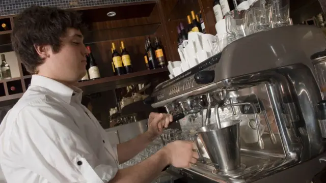 A man in a white shirt stands at a coffee machine.
