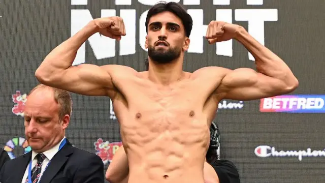 Adam Azim holds up his arms and is shirtless