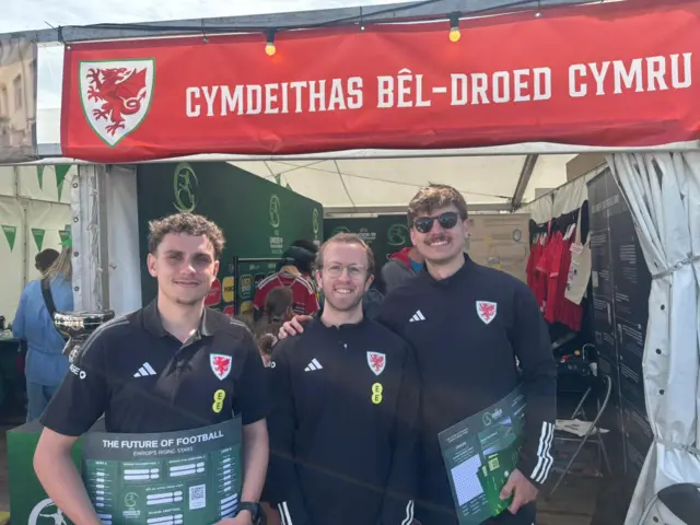 Tri dyn o flaen stondin Cymdeithas Bel-droed Cymru