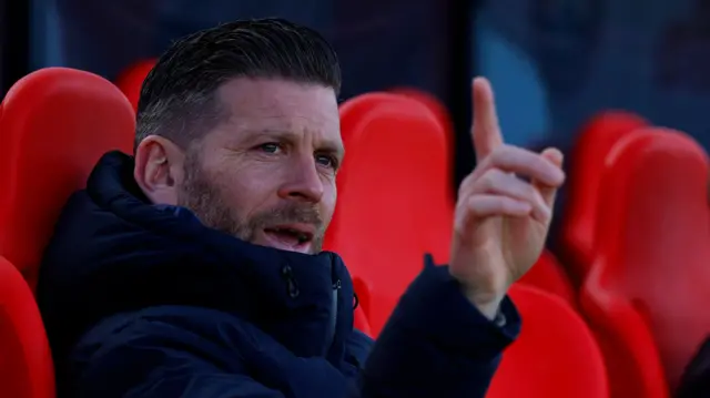 Boreham Wood boss Luke Garrard sat in the dugout and pointing one finger upwards