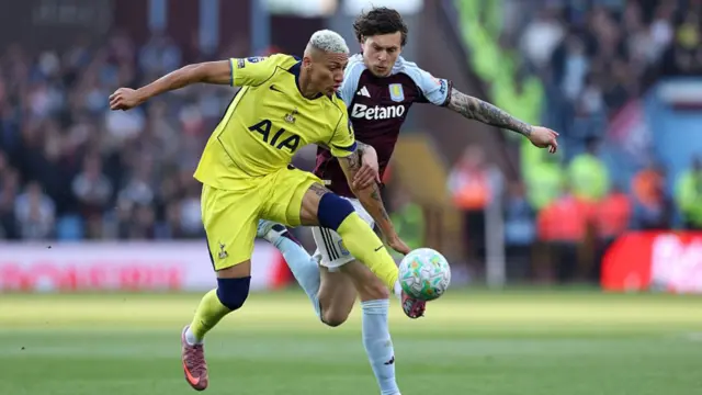A player in bright yellow kit with red boots contests a Villa player in Burgundy and light blue kit