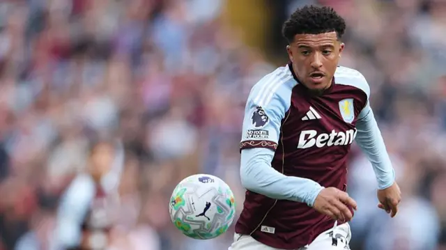 Jadon Sancho is focused on the ball as he runs toward it in a light blue and burgundy top