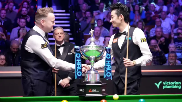 Shaun Murphy and Wu Yize shake hands next to the World Championship trophy
