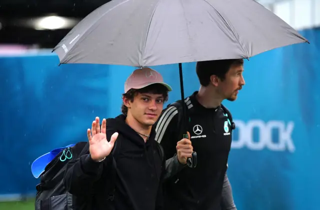 Kimi Antonelli, who is holding an umbrella, waves as he arrives at the circuit before the Miami Grand Prix