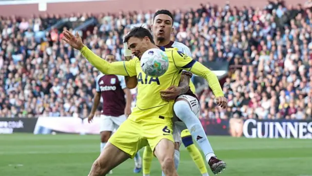 Morgan Rogers in a blue and red kit challenged by a Spurs player in bright yellow kit