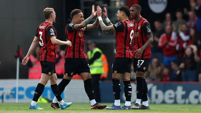 Bournemouth players celebrate a goal in black and red stripe kit