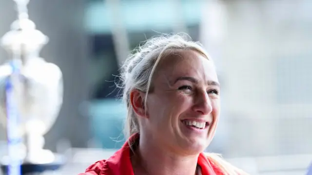 St Helens and England Women captain Jodie Cunningham smiling with the Challenge Cup trophy behind her in the background.