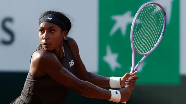 Coco Gauff, wearing a black dress, lines up for a backhand with her pale purple racquet drawn back in two hands to her left