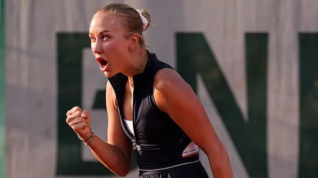Potapova, wearing a black dress with her blonde hair tied back in a bun, clenches her right fist in celebration and roars