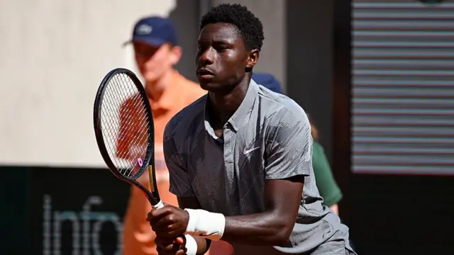 Moise Kouame, wearing a grey t-shirt, holds his racquet in front of himself in two hands