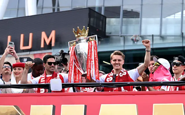 Mikel Arteta, Manager of Arsenal, and player Martin Odegaard hold the trophy and cheer on the top of the bus
