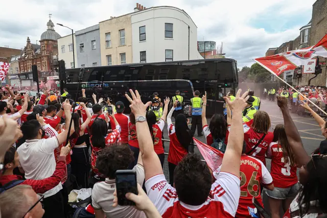Rows of fans cheer as a bus drives through north London