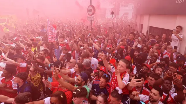 Arsenal supporters cheer their team as it passes during the victory parade for Arsenal's men team's Premier League title victory, around the streets near to the Emirates Stadium