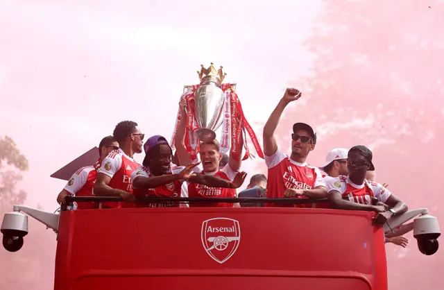 Martin Odegaard holds the trophy up on the open top Arsenal bus, as teammates celebrates next to him