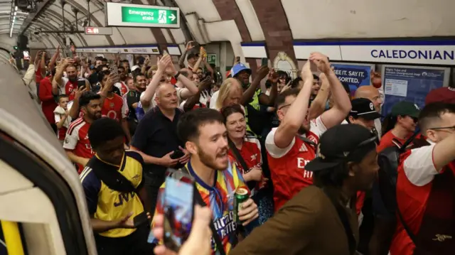 Large crowd of Arsenal fans celebrating inside Caledonian Road underground station, many filming on phones