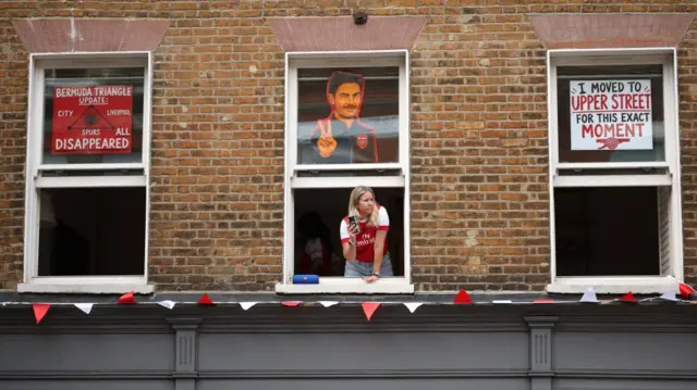 A fan leans out a window to take photos of the parade.
