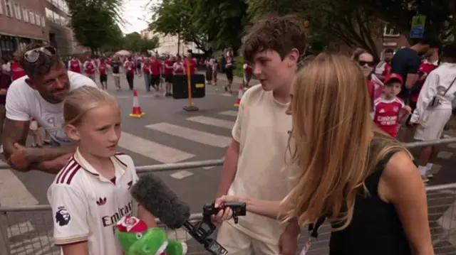 A young boy and young girl speak to a BBC reporter along the parade route