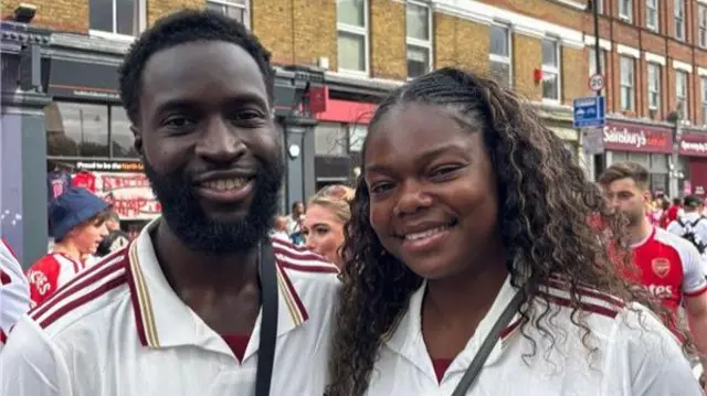 Michael and Teju pose for a picture. they both wear white arsenal jerseys.