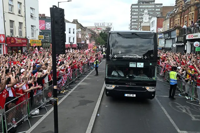 A black bus driving through with lines of Arsenal fans cheering on either side