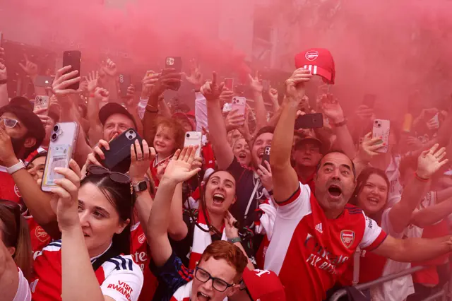 A view of fans watching the bus pass by, looking shocked and filming with their phones, as the sky is painted red