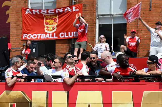 Arteta looking up towards the sun, sat on the top deck of the Champions bus