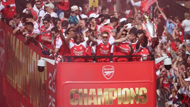 Arsenal's Viktor Gyokeres stands with his arms open wide and Saka holds up the trophy as parade passes surrounded by crowds