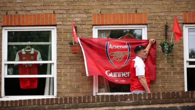 An Arsenal fan holding up an Arsenal flag on a window
