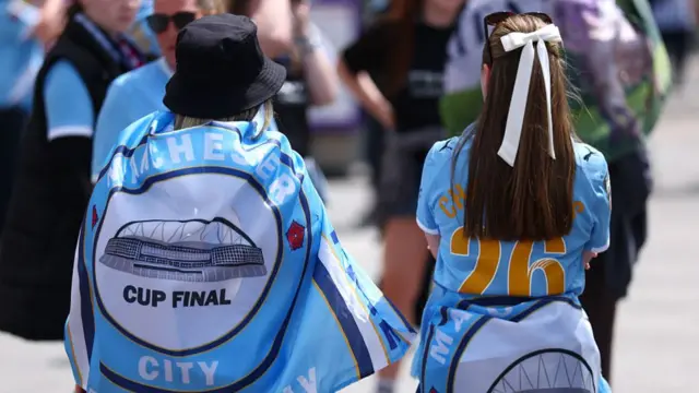 Fans of Manchester City, wearing FA Cup Final flags, make their way down Wembley Way