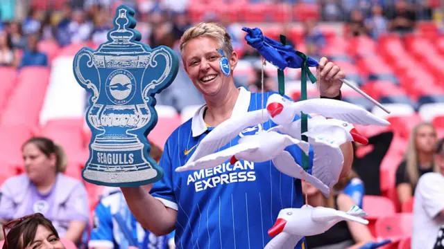 A fan of Brighton & Hove Albion holding inflatable seagulls and a foam FA Cup trophy replica