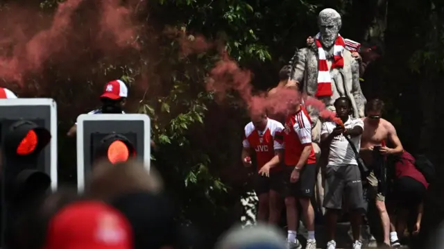 Arsenal fans celebrate on a statue of a man, and have put a scarf around its neck