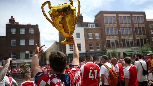 A man holds up a balloon shaped like the Premier League trophy
