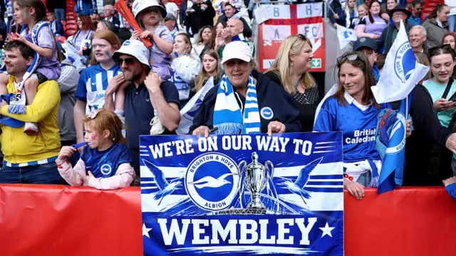 A fan of Brighton & Hove Albion poses for a photo with a sign which reads 'We're on our way to Wembley'