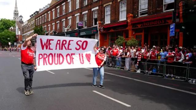 Fans hold up a banner that says "we are so proud of you"