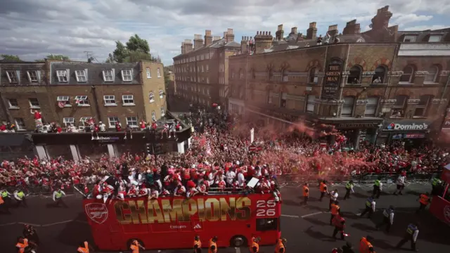 Fans watch on from balconies and windows as the buses pass by - red smoke comes from the crowd below